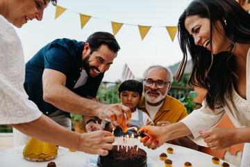Family lighting birthday cake candles at an outdoor party