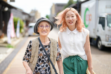 Fototapeta premium Two women, one with a hat and glasses, are walking down a street. The woman with the hat is smiling and the other woman is wearing a pink shirt