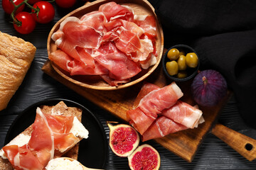 Plate with delicious prosciutto slices, figs and olives on black wooden background