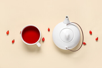 Cup and teapot of hot rose hip tea on beige background