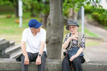 Obraz premium Two elderly people sitting on a stone wall, one wearing a blue hat. They are talking to each other