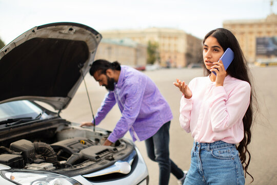 Frustrated Indian woman calling for help while man checks broken car engine. Scene shows teamwork, stress, and action in roadside emergency or breakdown situation, closeup