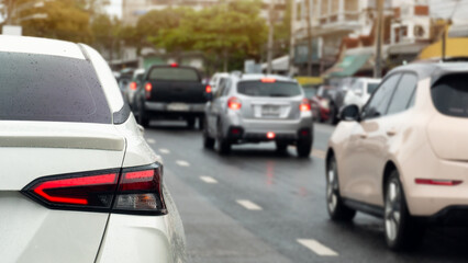 Fototapeta premium Rear side of luxury car driving on the asphalt road. On body of car with drop of water rain with turn on brake light. Blurred of cars driving in line on the wet asphalt road. Background of city.