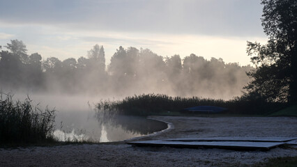 early autumn morning by the lake, fog hides the outlines of trees and bushes, blurred background