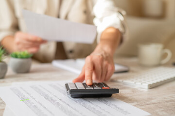 Woman focusing on calculating expenses and managing family budget, using a calculator and financial documents on a home office desk, planning for future savings and financial stability