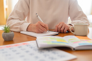 Woman's hands writing notes in a physical planner or journal, organizing daily activities and appointments for improved productivity and a balanced lifestyle at a home office desk