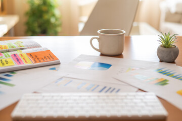 Home office desk with financial charts, notebook with colorful sticky notes, coffee mug and potted plant, workspace for budgeting, accounting, planning and remote business analysis