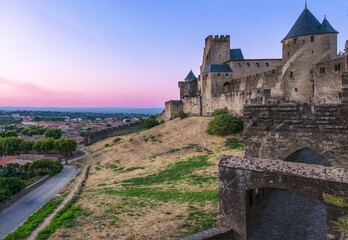 Medieval fortress walls and towers of Carcassonne at sunset, France. Old medieval walls of Carcassonne illuminated by purple sunset sky.