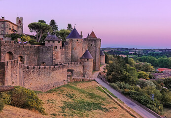 Medieval fortress walls and towers of Carcassonne at sunset, France. Old medieval walls of Carcassonne illuminated by purple sunset sky.