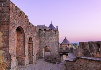 Medieval fortress walls and towers of Carcassonne at sunset, France. Old medieval walls of Carcassonne illuminated by purple sunset sky.
