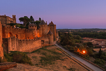 Medieval fortress walls and towers of Carcassonne at sunset, France. Old medieval walls of Carcassonne illuminated by purple night sky.
