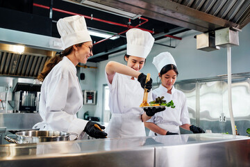 Team of chefs in white uniforms and toques plate gourmet dish in commercial kitchen. Scene shows...
