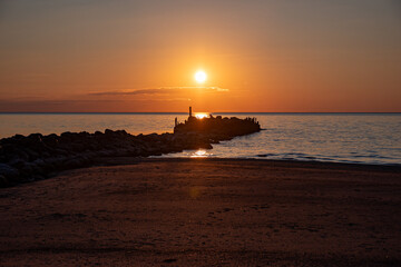 Magical sunset by the sea, old stone pier, the last rays of the sun reflected in the calm sea...