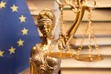 Golden lady justice statue holding scales in front of European Union flag and books in a law office...