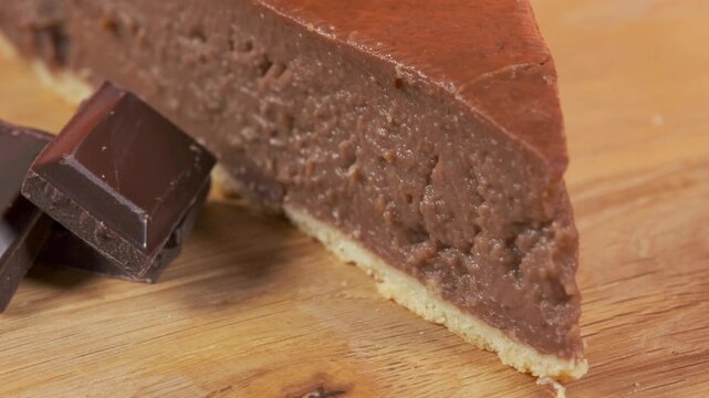  Slice of French chocolate flan on rotating wooden table with chocolate bar pieces, orange background, close-up food footage.