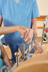 Close-up view of unrecognizable aged female patient training fine motor skills on rehab equipment in neurological hospital under control of nurse