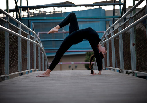 Woman practicing yoga bridge pose on urban bridge
