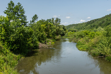 Obraz premium Serene river winding through lush greenery under a clear sky during daytime at a rural landscape