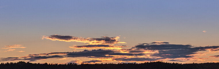 Colorful sunset over a forested landscape with clouds reflecting warm hues in the evening sky during twilight hours
