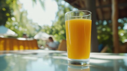 A glass filled with bright orange juice sits on a polished surface, with small oranges in the background, capturing the lively atmosphere of a bar in daylight.