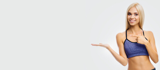 Wide banner image - happy woman wear blue purple fitness sportswear showing free ad sign space. Smiling fit cute blond girl pointing side away mockup empty text, isolated bright grey background