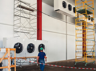 Man walking in industrial refrigeration room with scaffolding and equipment.