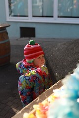 Little girl in colorful winter clothes and striped hat gazes at festive display at Christmas market, lit by sunlight