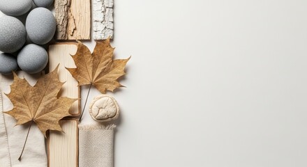 Composition of natural elements: grey stones, wood textures, and dried maple leaves on a white background with copy space.