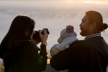 Parents and their little child pose for a photo on a misty mountain peak, enjoying warm sunlight in the winter season.
