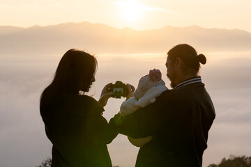 Parents and their little child pose for a photo on a misty mountain peak, enjoying warm sunlight in the winter season.