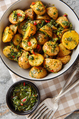 Golden roasted potatoes are tossed with a bright and peppery chimichurri sauce closeup on the plate on the table. Vertical top view from above
