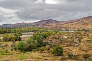 Fototapeta premium A desolate landscape near the Uplistsikhe Cape Town in Georgia with a river running through it. The sky is cloudy and the sun is not visible in autumn.