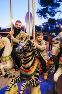 Father and son riding carousel horses at Plaza de Col�n Madrid in evening