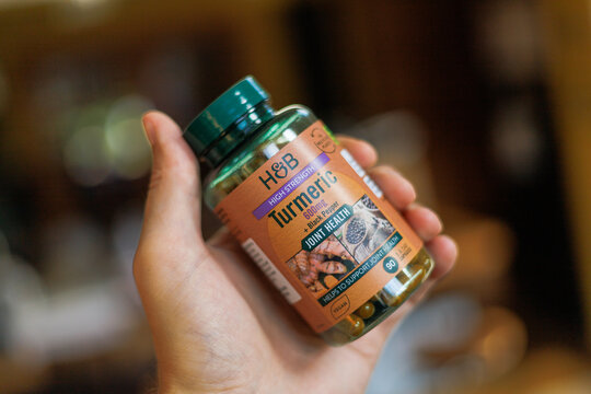 A bottle of Holland & Barrett turmeric capsules held in a hand, set in a warm, natural lifestyle environment that emphasises daily wellness, herbal nutrition, and holistic self-care
