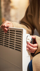 Person turning thermostat knob on electric heater to adjust temperature. Concept of home energy...