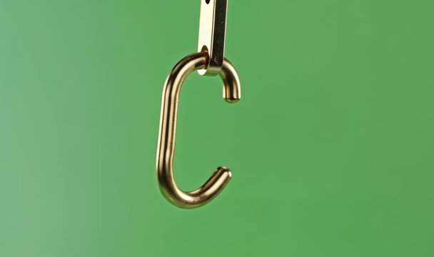 Close up of a golden hook hanging against a green background.