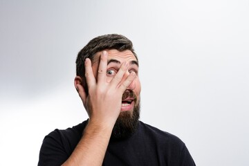 Obraz premium Man peeking through fingers with surprised expression.