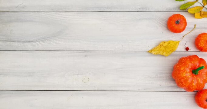 Autumn composition with pumpkins and fallen colorful leaves on white wooden background with place for text. 4K looped stop motion animation