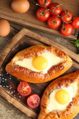 Tasty khachapuris with cheese, eggs and tomatoes on wooden table, flat lay