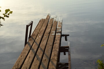 An old wooden pier. An old wooden walkway stands on rusty iron supports in the water. The wood has...