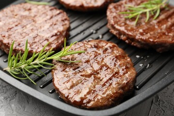 Pan with grilled patties and rosemary on grey table, closeup