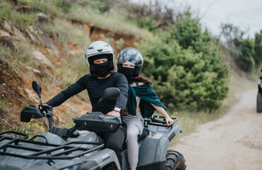 Two people wearing helmets and protective gear ride a quad bike along a scenic hillside trail...
