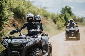 A group of friends drives all-terrain quad bikes on an off-road forest path, showcasing adventure, teamwork, and outdoor exploration surrounded by lush greenery under a bright blue sky. © qunica.com