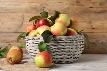 Fresh ripe apples with green leaves in wicker basket on white wooden table