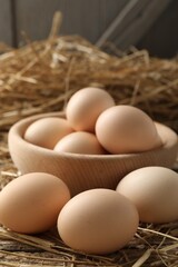 Raw chicken eggs in bowl and straw on wooden table, closeup