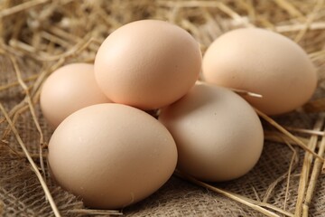 Raw chicken eggs and straw on table, closeup