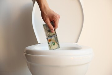 Man throwing dollar banknote into toilet bowl near white wall, closeup