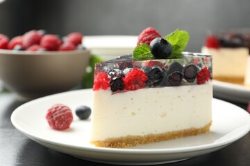 Piece of delicious cheesecake with berries and mint on black wooden table, closeup