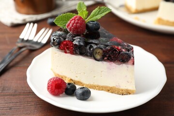 Piece of delicious cheesecake with berries and mint served on wooden table, closeup