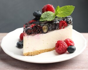 Piece of delicious cheesecake with berries and mint on wooden table, closeup